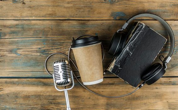 old book with headphone and a cup of coffee in a disposable paper cup on a wooden table. Remote education concept. Top view