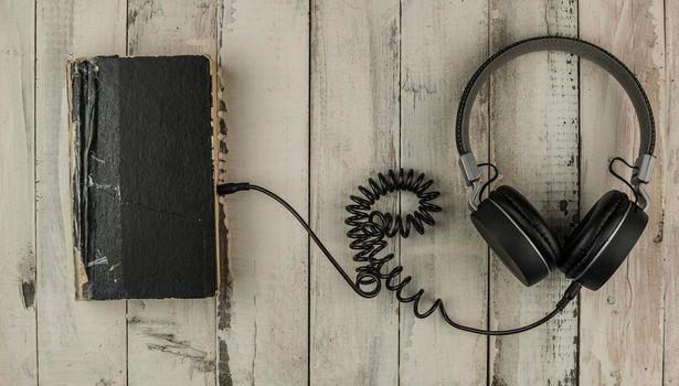 Audio book concept. Headphones and old book over wooden table. Top view with space for your text. Remote education concept.