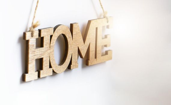 Home wood decorative lettering hanging on a white wall illuminated by sunlight. Home Interior and copy-space. Selective focus