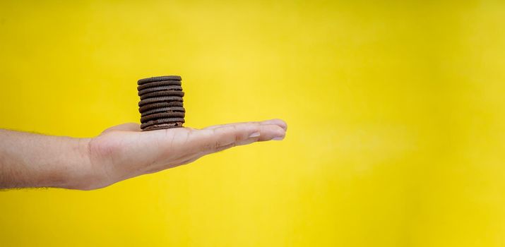 hands holding chocolate biscuits on a yellow background with copy space