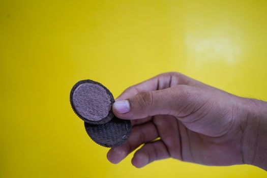 hands holding chocolate biscuits on a yellow background with copy space