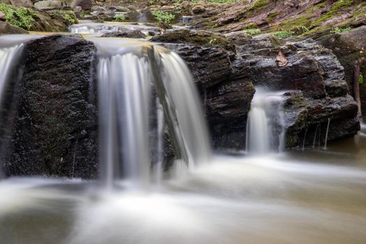 Beautiful softness in the texture of the long exposure spilling water juxtaposes with the roughness of the rocks it falls over. SDhot in natural dappled woodland light with copy space and no people. Idyllic nature background environmental scene.