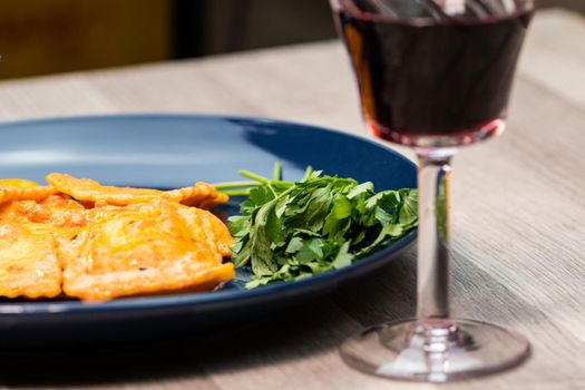 glass of red wine in front of a plate of ravioli with fish