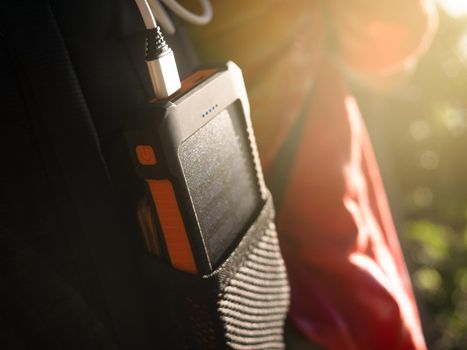 A rechargeable mobile power pack with solar panels in young female traveler's backpack, close-up. Connected to and charging a mobile, tablet or smart phone.