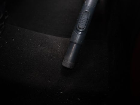 Close up of hands vacuuming car mat with vacuum cleaner inside a dark and dirty car.