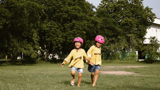 Two cute little sisters in helmet running on the lawn in park on a sunny summer day, taking a break after cycling practice. Happy childhood. Family spending time together.