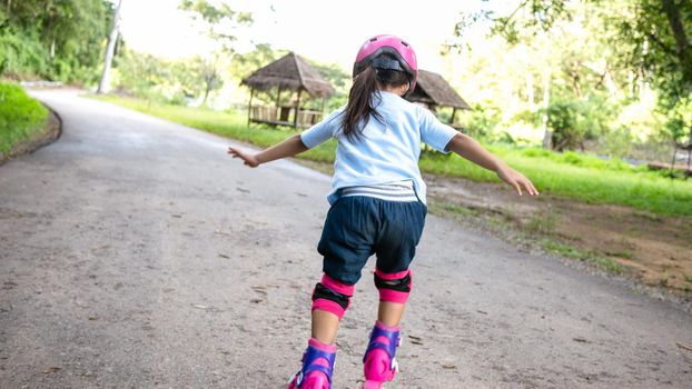 Little girl wearing protection pads and safety helmet learning to roller skate in summer park. Active outdoor sport for kids.