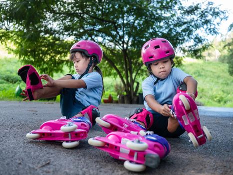 Two sibling sisters wearing protection pads and safety helmet practicing to roller skate on the street in the park. Active outdoor sport for kids.