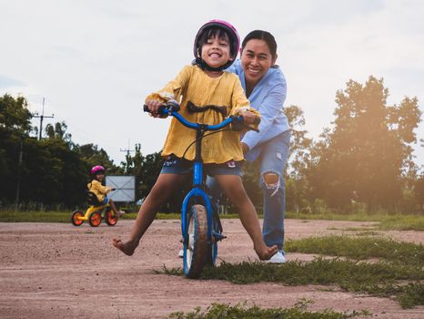 Cute little girl in safety helmet learn to ride a bike with her mother in summer park. Outdoor sports for kids. childhood happiness. family spending time together.