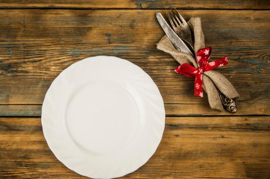 Festive composition with empty white plate and cutlery set on rustic wooden table. Christmas holiday. Top view