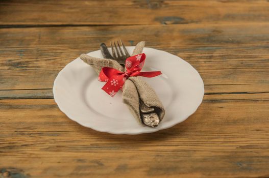 Festive composition with empty white plate and cutlery set on rustic wooden table. Christmas holiday.
