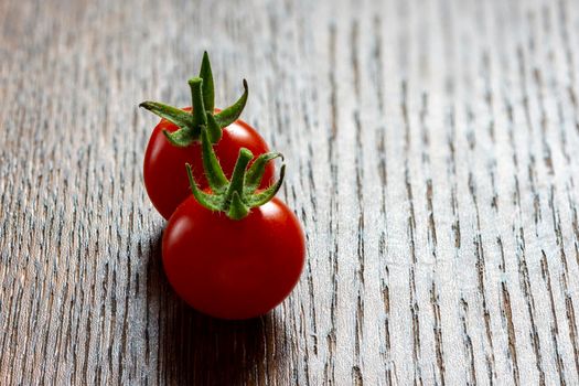 Two small, red cherry tomatoes lie on a wooden table