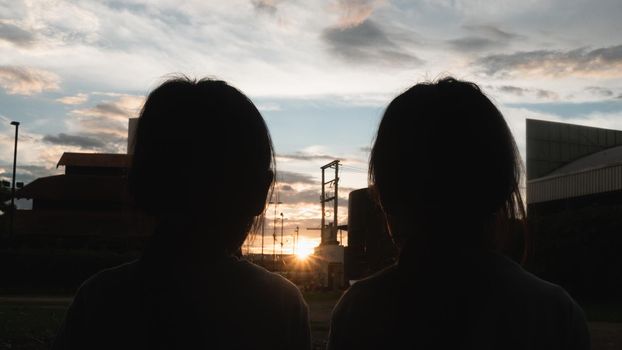 Two sibling sisters eating sweet tasty ice cream outdoors at sunset. Two happy young kid enjoy dessert during vacation holiday in the park.