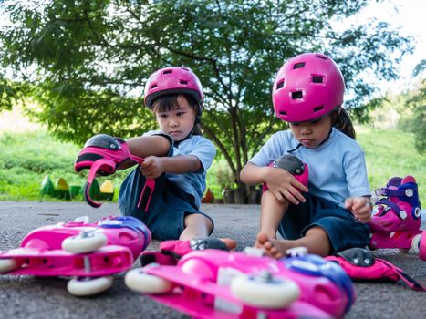 Two sibling sisters wearing protection pads and safety helmet practicing to roller skate on the street in the park. Active outdoor sport for kids.