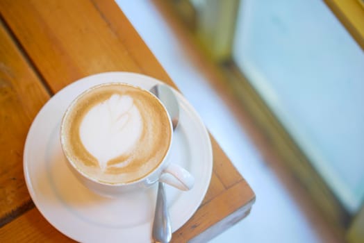 a cup of late coffee with flower shape design on top at cafe .