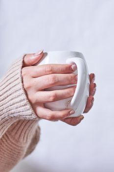 Female hand holding hot tea cup against white background. A woman in warm knitted sweater holds in hands tasty herbal tea