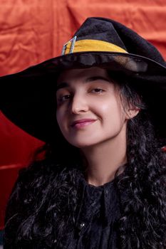 Portrait of a cute multi-racial woman in witch cap against orange background. Studio shot. Close-up shot of female in witch costume