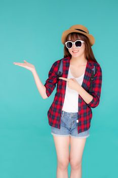 Beautiful portrait young asian woman wear sunglasses and hat smile and enjoy in summer gesture presenting and pointing something isolated on blue background, tourist girl in vacation travel concept.