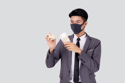 Young asian businessman in face mask holding money Thai and home isolated on white background, pandemic and crisis of economic, business man and investment property during disease covid-19.