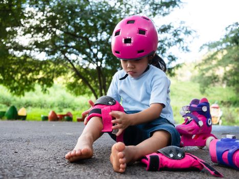 Cute little girl wearing protection pads and safety helmet practicing to roller skate on the street in the park. Active outdoor sport for kids.