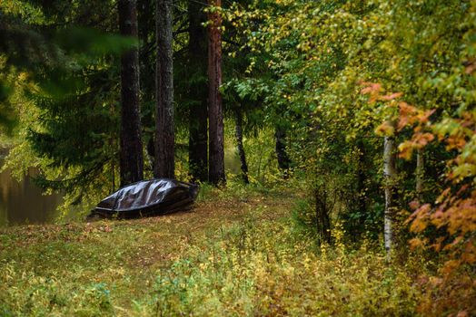 An old metal boat is made with your own hands on the shore of the lake in the autumn season.