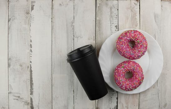 Donut on a plate and  disposable cup of coffee on a wooden table. Photo of sweets. Top view. Copy space. Mock-up 