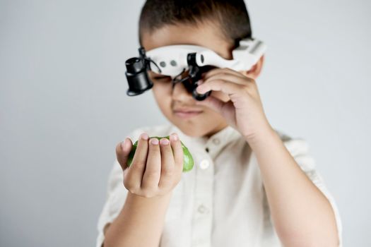 Little boy holding a slime and looking on it through the special magnifying eyeglasses headset