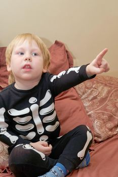 A child in a skeleton costume sits on the couch and points his finger forward. Children fears and horror stories