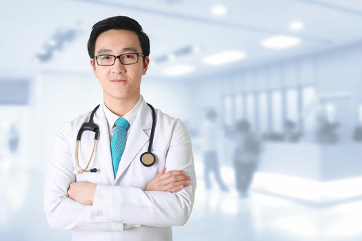 Doctor posing with arms crossed, medical staff working on blurry background.