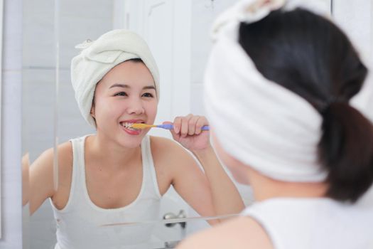 Young asian woman brushing her teeth at the mirror.