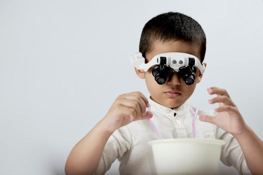 Portrait of a cute kid in magnifying eyeglasses headset experimenting with liquids against the white background