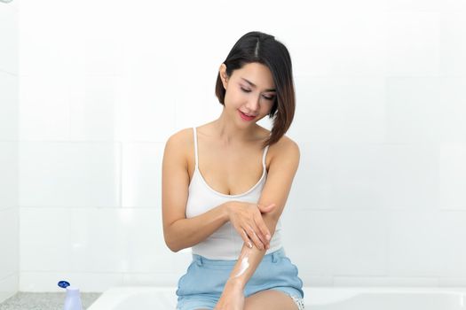 Young woman applying body lotion cream after bath.