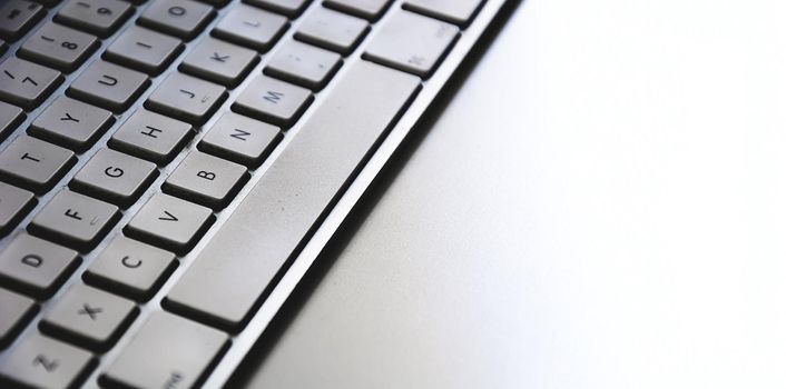 Detail of a modern white computer keyboard dirty and dusty on a white table. Computer hardware device. Technology and internet