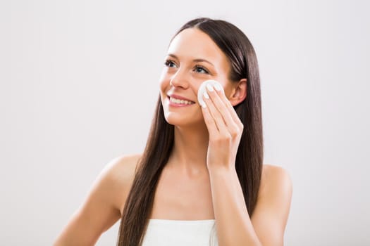 Beautiful brunette woman cleaning her face with cotton pad.