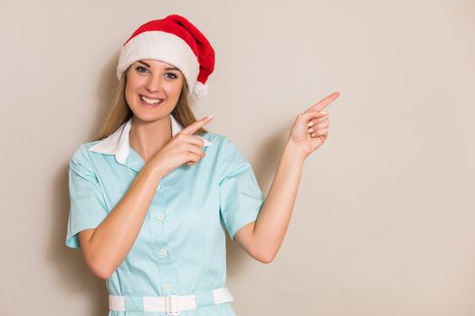 Portrait of nurse with Santa hat looking at camera and pointing.