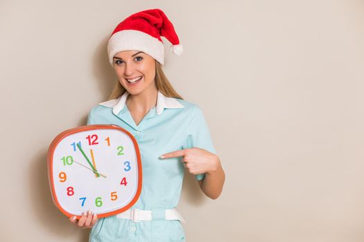 Portrait of nurse with Santa hat pointing at clock.