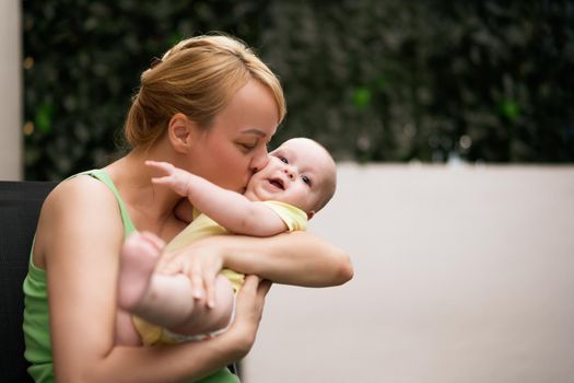 Mother enjoys holding and kissing her little cheerful baby boy.