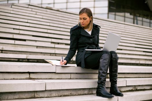 Beautiful businesswoman sitting on the staircase in the city and working.