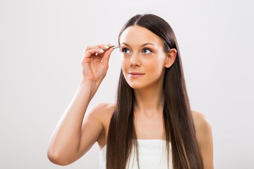 Image of beautiful brunette woman plucking eyebrows.