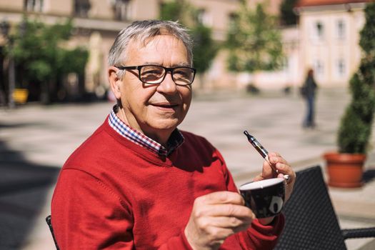 Cheerful senior man enjoys drinking coffee and smoking electronic cigarette at the bar.Image is intentionally toned.