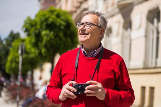 Senior man tourist enjoys photographing at the city.Image is intentionally toned.