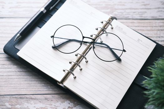 notepad, eyeglass and a pencil on wooden table .
