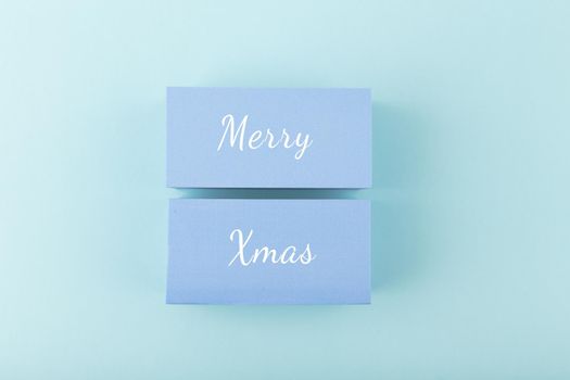 Merry Christmas minimal concept in light pastel blue colors. Handwritten text Merry Christmas on blue tablets against blue background. Modern trendy Merry Xmas concept