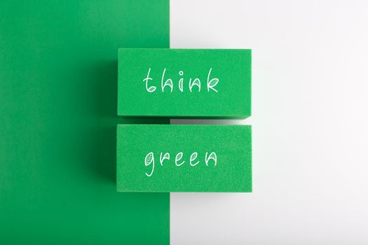 Modern minimal flat lay composition with think green inscription against green and white background. Concept of go green, recycle, reduce, reuse, zero waste and eco friendly lifestyle