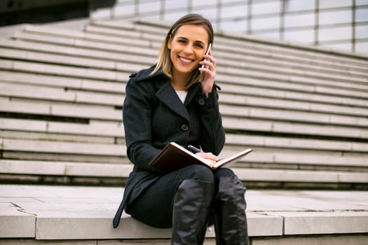 Businesswoman using phone and personal organizer while working outdoor.