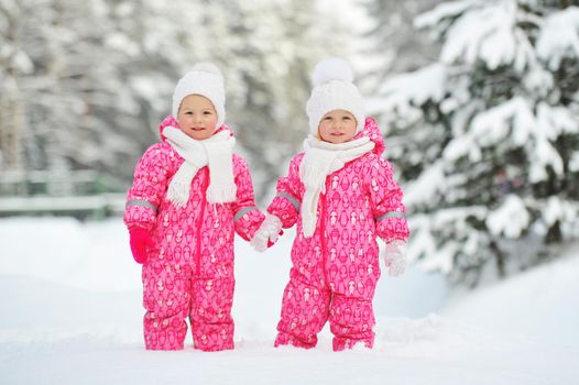 Two little twin girls in red suits stand in a snowy winter forest.