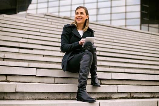 Beautiful businesswoman sitting on the staircase in the city and using digital tablet.