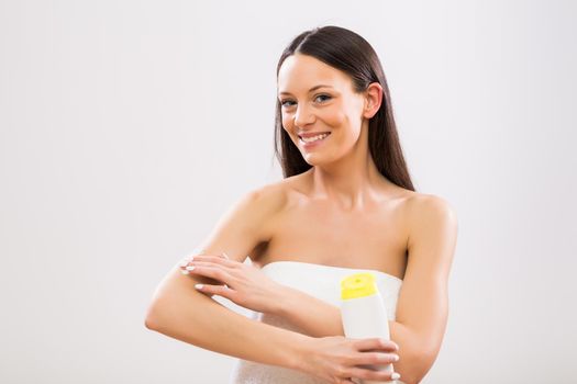 Beautiful woman applying moisturizer on her arm on gray background.