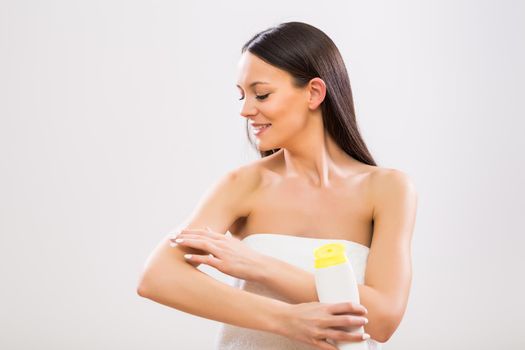 Beautiful woman applying moisturizer on her arm on gray background.