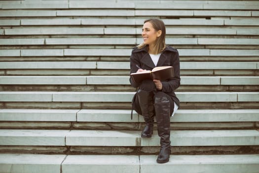 Beautiful businesswoman sitting on the staircase in the city and working.